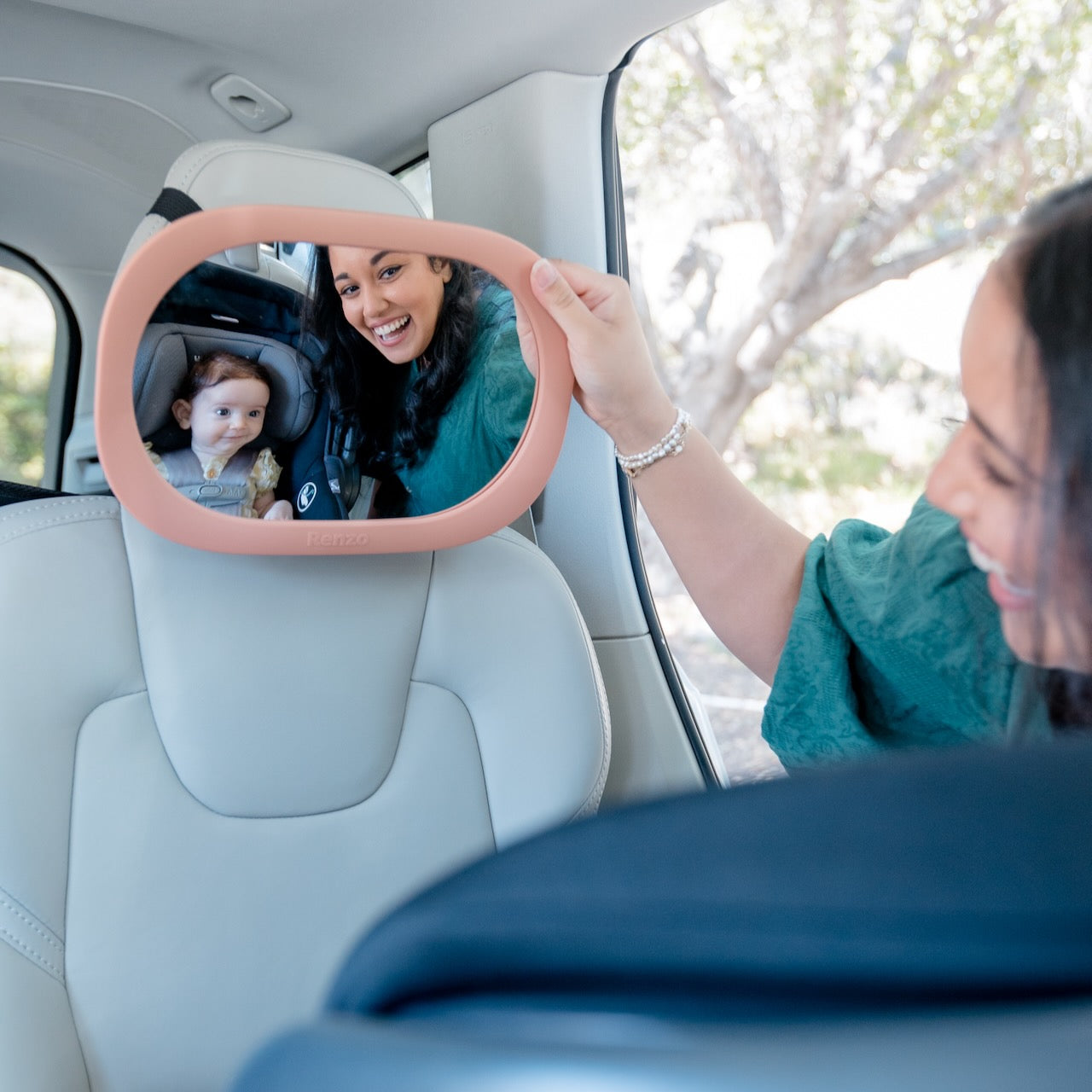 Parent smiling while adjusting a Blush Pink Renzo Baby Car Mirror to see their baby in a car seat.